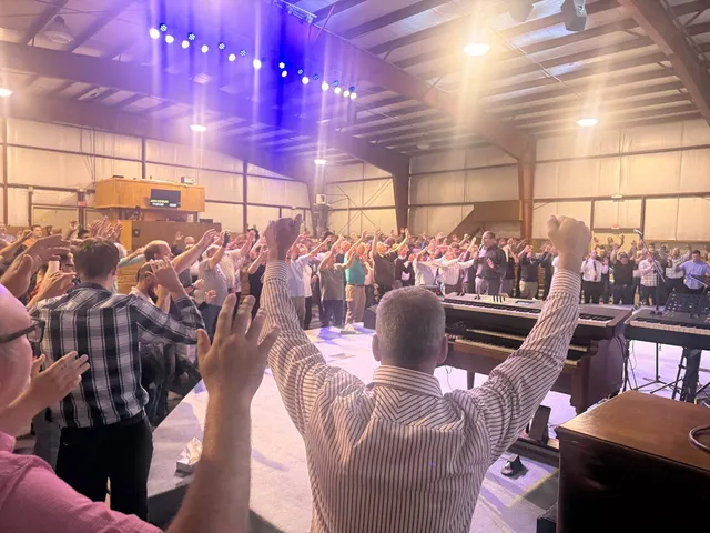 Men worship across the camp hall beside the organ and stage.