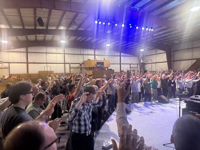 Side-stage view of rows of men worshiping beneath blue stage lights.
