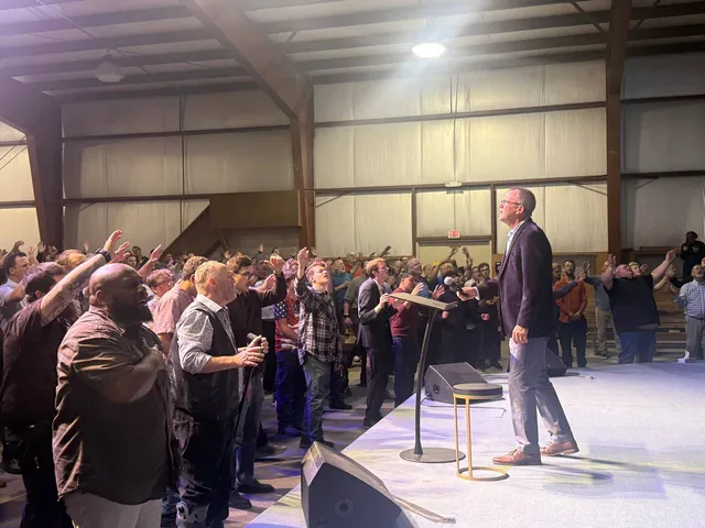 Men reach toward the stage while a speaker stands at the front.