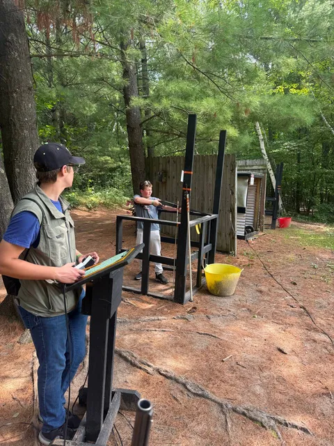 Two participants at a wooded clay-shooting station during camp recreation.