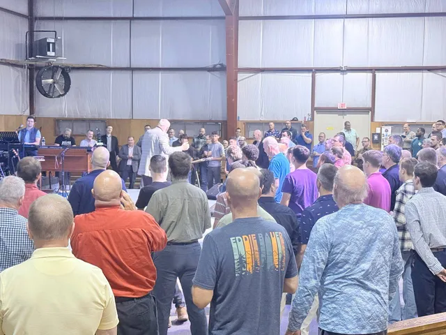 Wide rear view of a speaker ministering to men at the front.